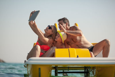 Midsection of man photographing woman with mobile phone while sitting in water