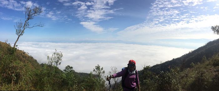 Female hiker standing on mountain by cloudscape against sky