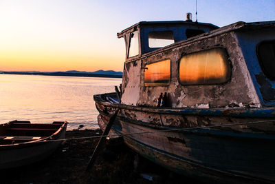 Abandoned boat moored on shore against sky during sunset