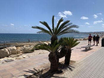 People walking on footpath by sea against sky