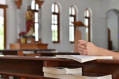Cropped hands of person praying over bible at church