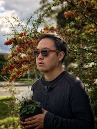 Portrait of young man holding potted white flowering cyclamen plant against yellow rowan berry tree.