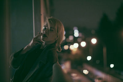 Portrait of woman standing by illuminated light at night