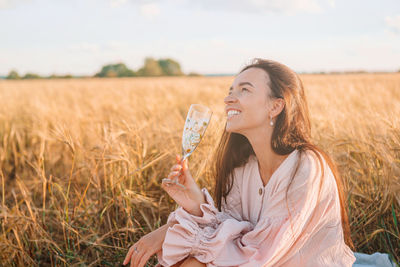 Smiling woman holding wine glass sitting on grass against sky