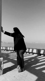 Side view of woman leaning on wall at walkway by sea against sky