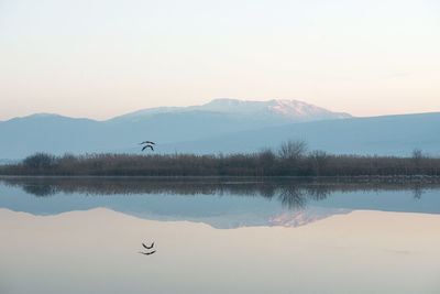 Scenic view of calm lake by mountains against sky at morning