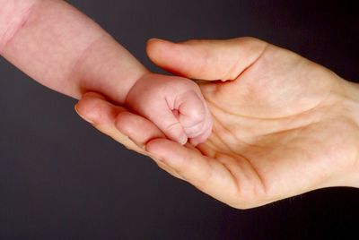 Cropped hand of mother holding baby against black background