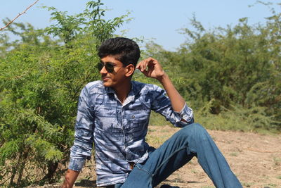 Young man sitting on land against trees