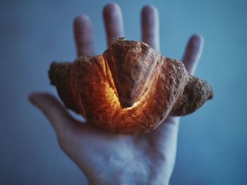 Close-up of hand holding croissant against white background
