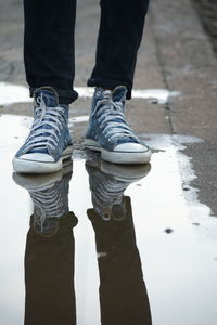 Low section of person standing by puddle at railroad station platform