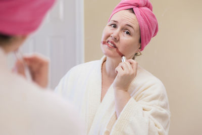 Mature woman applying lipstick reflecting on mirror