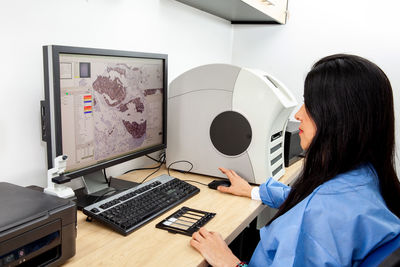 Young female scientist scanning microscope slides with tissue samples for pathology studies. 