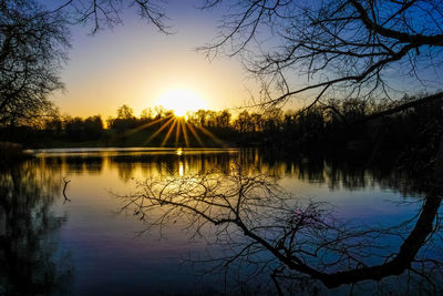 Silhouette trees by lake against sky during sunset