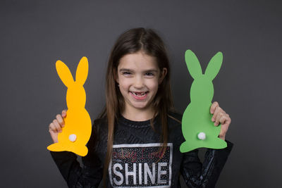 Portrait of smiling girl holding paper eater bunny against gray background