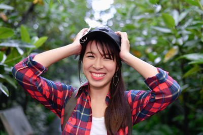 Portrait of smiling young woman standing against trees