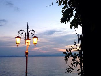 Illuminated street light by sea against sky