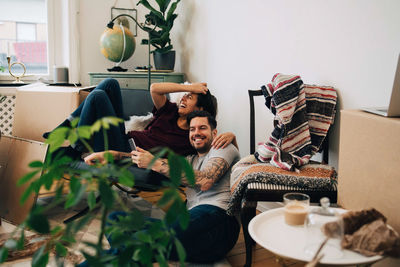 Happy couple using smart phone while resting at new home during location