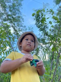 Portrait of cute girl holding plant against trees