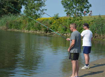 Men fishing on lakeshore against plants