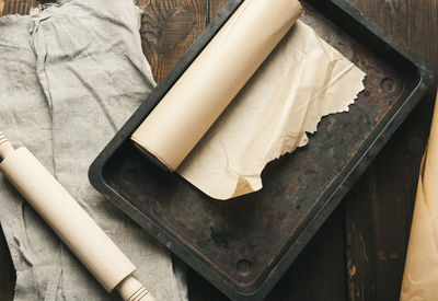 Empty rectangular metal pan covered with brown parchment paper and paper rolls on a woode