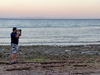 Man photographing sea against sky during sunset