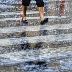Low section of man standing on wet road during rainy season