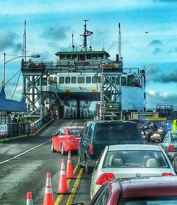 Cranes at harbor against cloudy sky