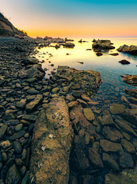 Surface level of rocks at shore against sky during sunset