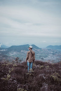 Rear view of man standing on mountain against sky