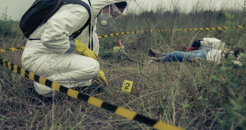 Detective wearing protective suit crouching on land at crime scene