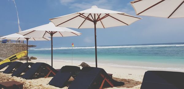Deck chairs and parasols on beach against sky