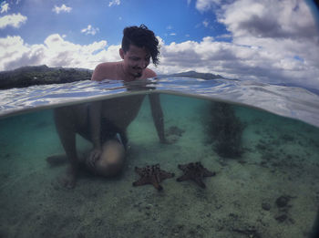 Man sitting in sea by starfish against sky