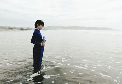 Boy standing in sea against sky