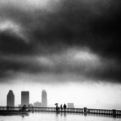 People walking in city against cloudy sky