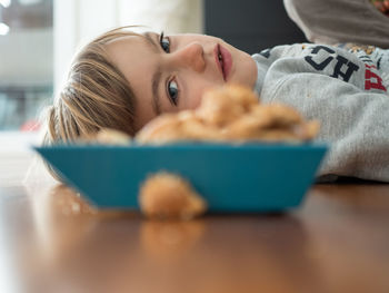 Boy lying by cereal bowl on floor at home