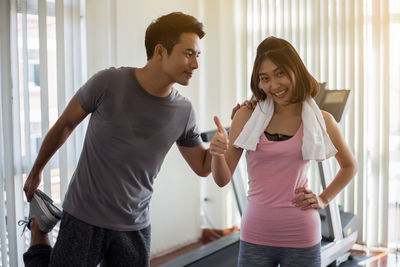 Portrait of smiling woman gesturing thumbs up sign with friend in gym