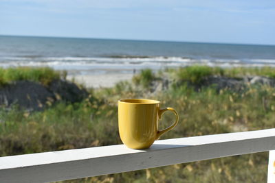 Close-up of coffee on handrail against sea