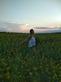 Young woman standing amidst plants on field against sky during sunset