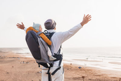 Rear view of man standing at beach against clear sky