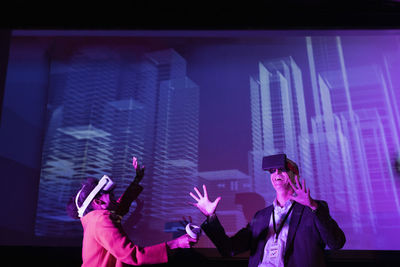 Happy male and female entrepreneurs with futuristic glasses gesturing by projection screen at convention center