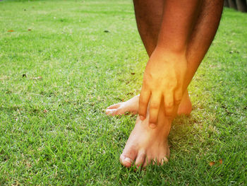 Low section of person scratching leg while standing on grassy field