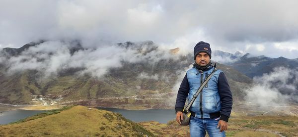 Portrait of young man standing on mountain against sky