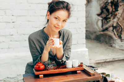 Young woman preparing green tea while sitting against wall