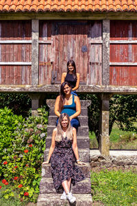 View of smiling women sitting on staircase against log cabin