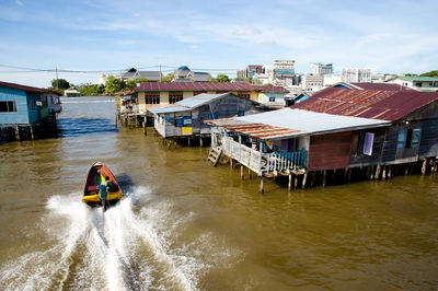 People on river amidst buildings against sky