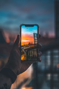 Close-up of hand holding smart phone against sky