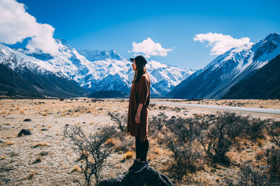 Rear view of man standing on snowcapped mountain against sky