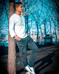 Side view of young man looking away while standing against tree trunk