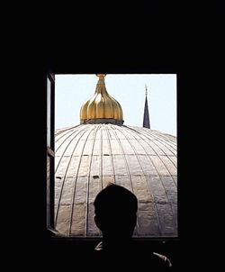 Rear view of silhouette man looking through window in building