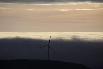 Silhouette wind turbines on field against sky during sunset